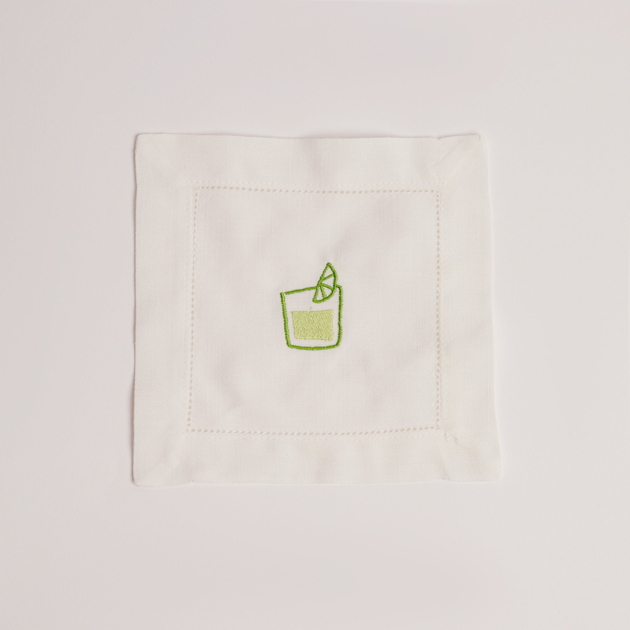 Single white cocktail napkin embroidered with a green mojito glass and lime wedge. Single white cocktail napkin embroidered with a green mojito glass and lime wedge.