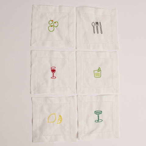 A set of white cocktail napkins with various embroidered designs including a glass of red wine, a lemon, an orange, a cucumber, and a cocktail glass. A set of white cocktail napkins with various embroidered designs including a glass of red wine, a lemon, an orange, a cucumber, and a cocktail glass.
