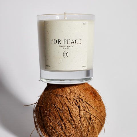 Boujie For Peace scented jar candle, handmade with natural soy wax, resting on a whole coconut – front view. Boujie For Peace scented jar candle, handmade with natural soy wax, resting on a whole coconut – front view.
