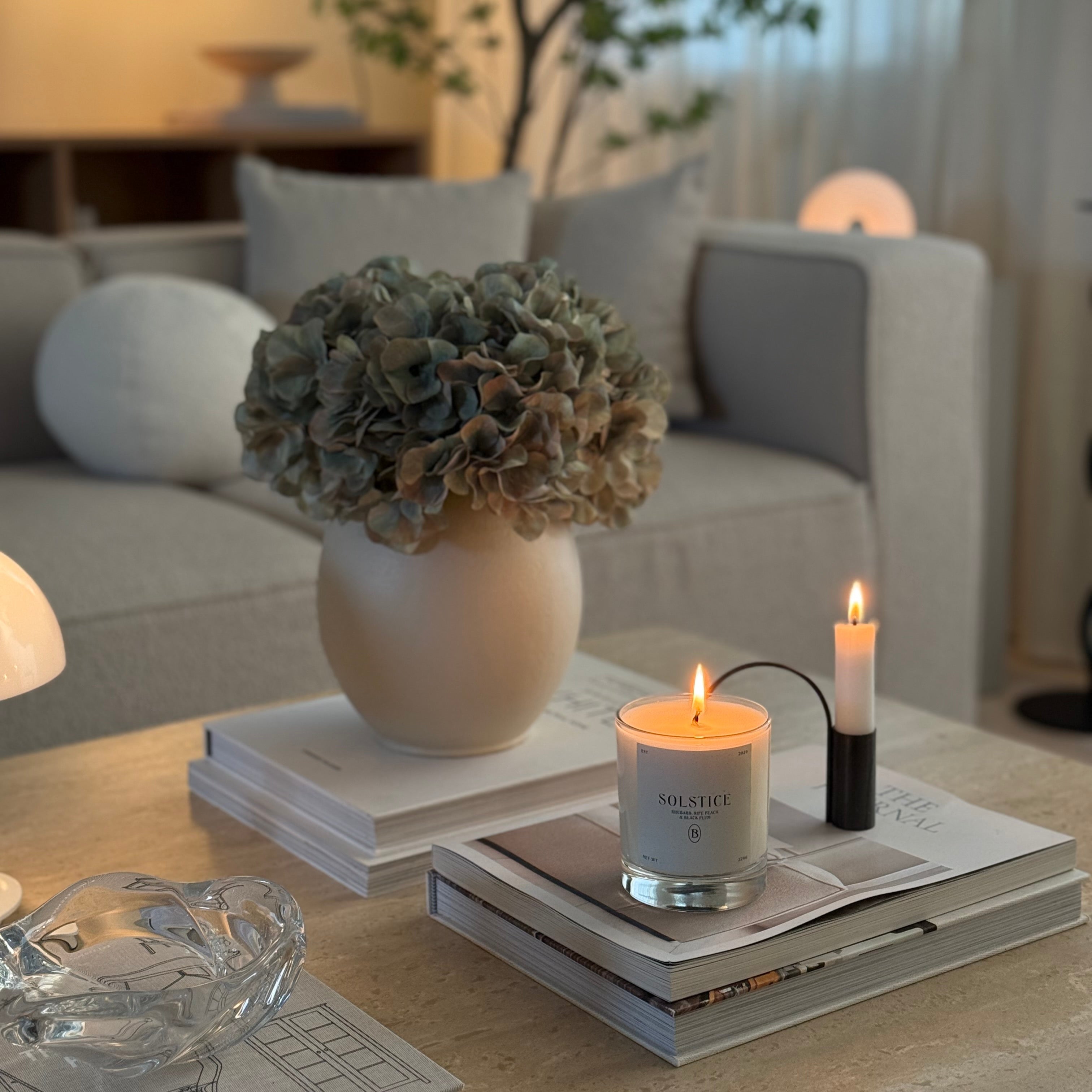 Boujie Solstice candle styled on coffee table with neutral decor, books and ceramic vase in a warm minimalist living room setting. Boujie Solstice candle styled on coffee table with neutral decor, books and ceramic vase in a warm minimalist living room setting.