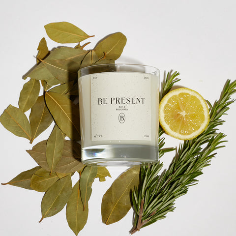 Boujie Be Present luxury soy wax jar candle, front view, handmade with natural soy wax in a clear glass jar, scented with bay and rosemary, surrounded by dried bay leaves, rosemary sprig, and lemon slice.