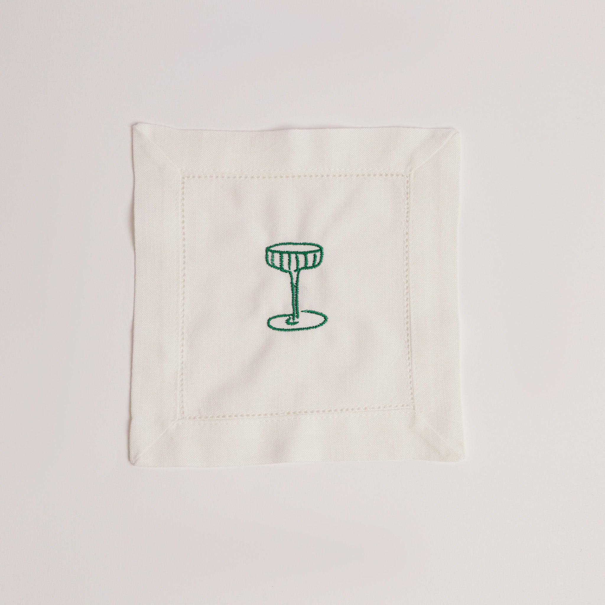 Single white cocktail napkin embroidered with a green cocktail glass.