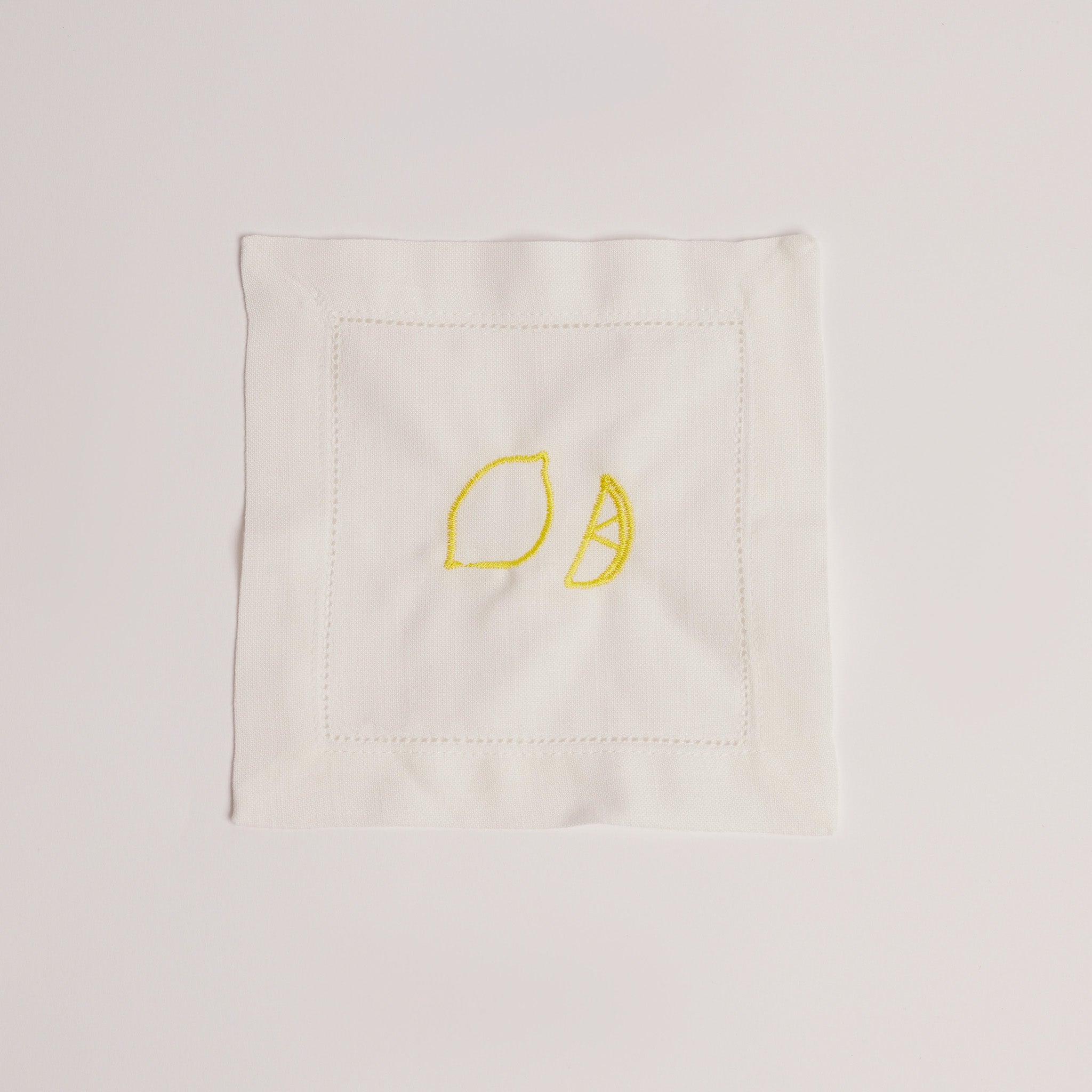 Single white cocktail napkin embroidered with a yellow lemon and lemon wedge.