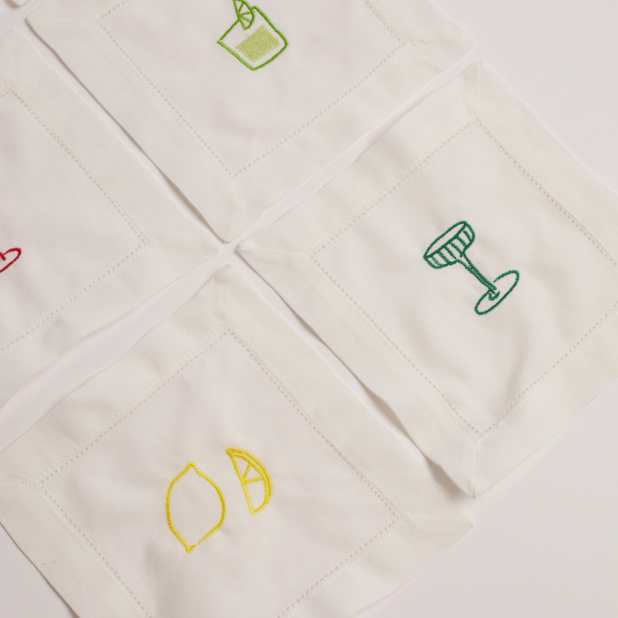 Set of white embroidered cocktail napkins with lemon, cocktail glass, and mojito glass designs.
