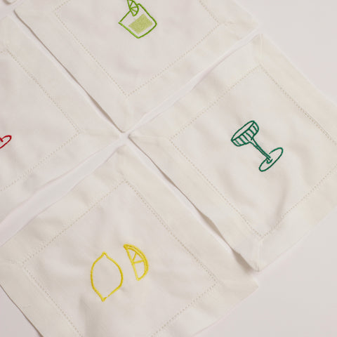 Set of white embroidered cocktail napkins with lemon, cocktail glass, and mojito glass designs.
