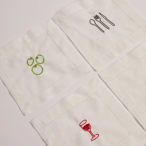 Set of white embroidered cocktail napkins featuring olive, cutlery, and wine glass designs.
