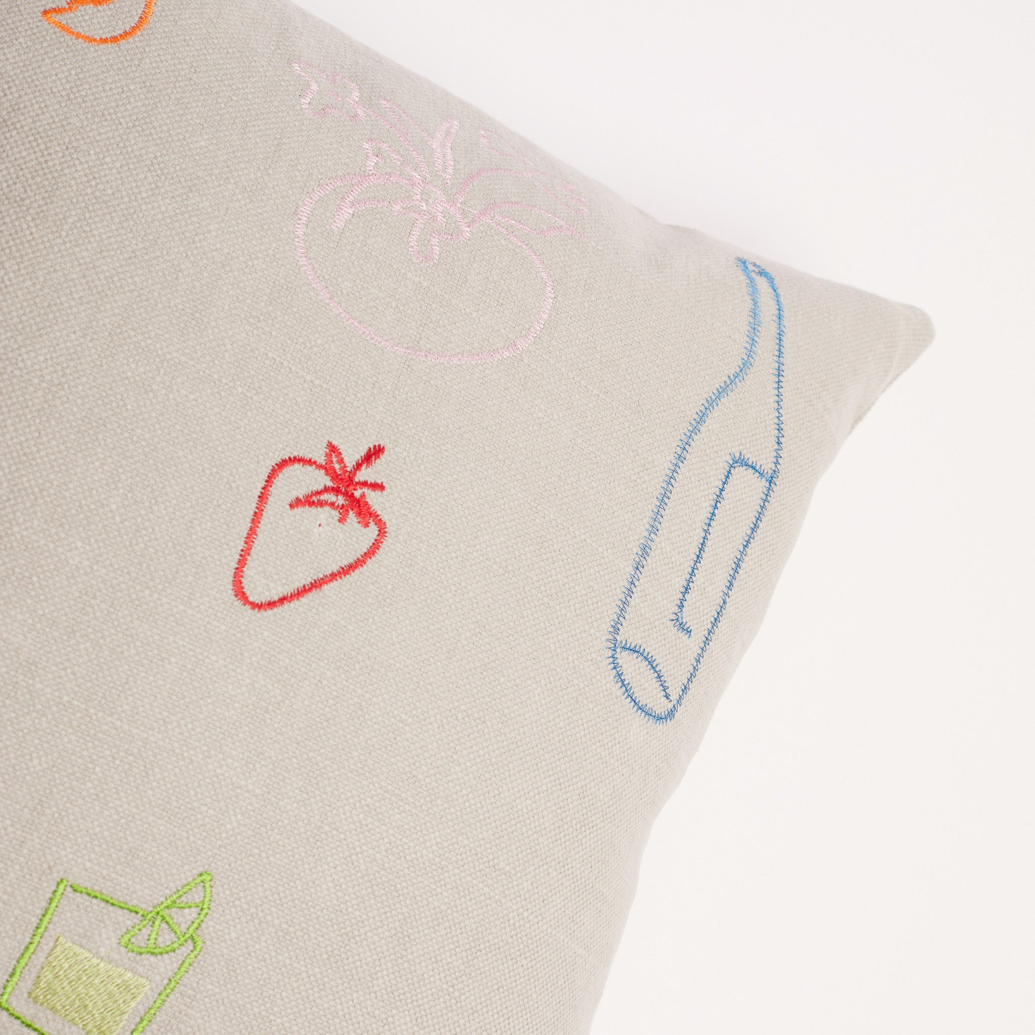 Close-up of blue bottle and red strawberry embroidery on neutral linen cushion.