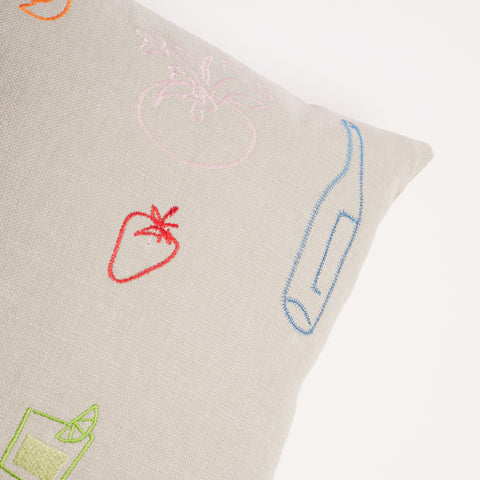 Close-up of blue bottle and red strawberry embroidery on neutral linen cushion.