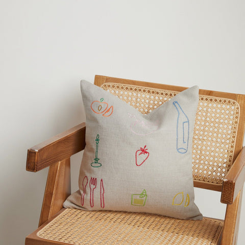 Detailed view of colourful embroidered designs on neutral linen cushion fabric.