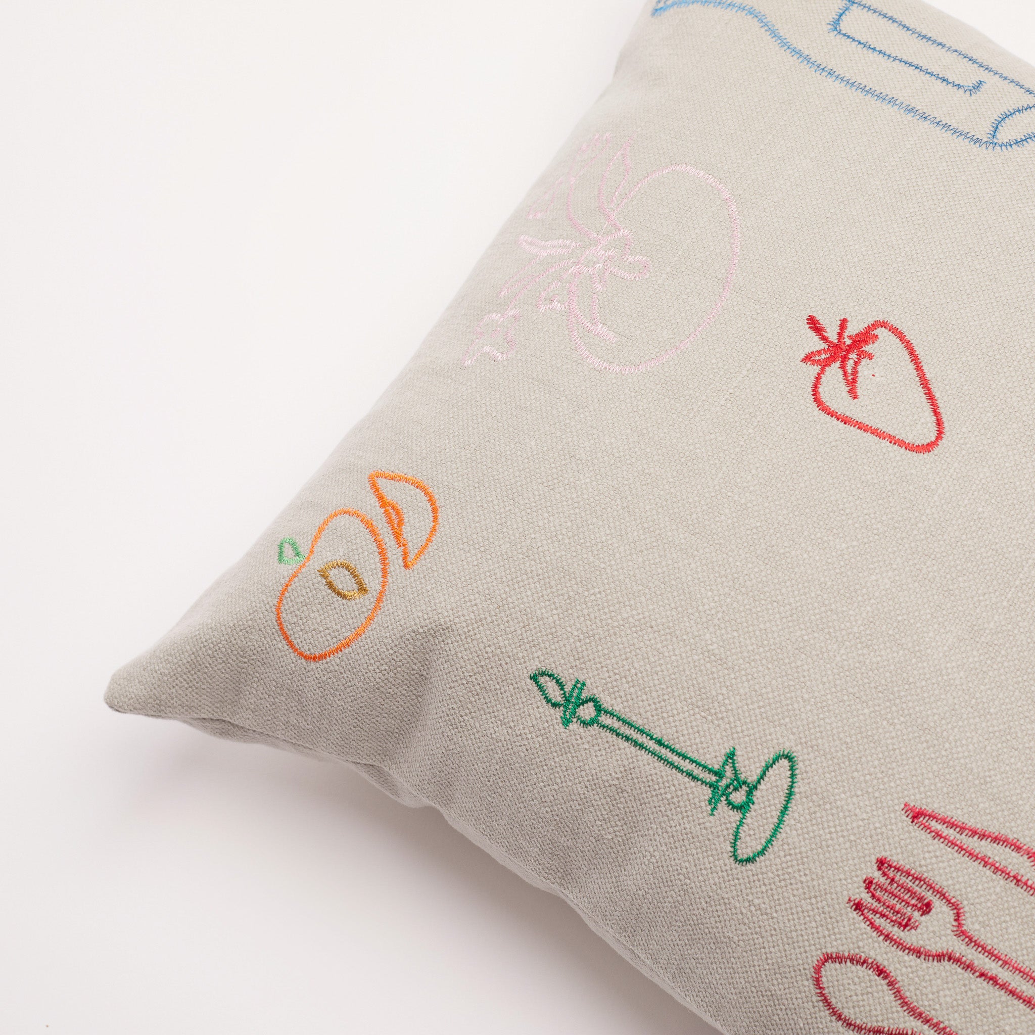 Detailed shot of orange and pink fruit embroidery on neutral linen cushion.