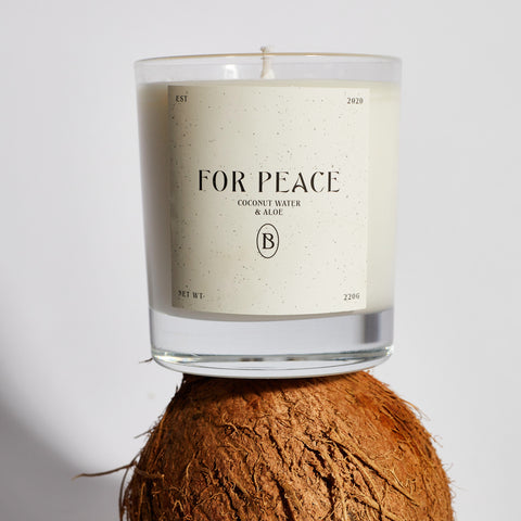 Boujie For Peace scented jar candle with coconut water and aloe fragrance, displayed on top of a whole coconut – close-up view.