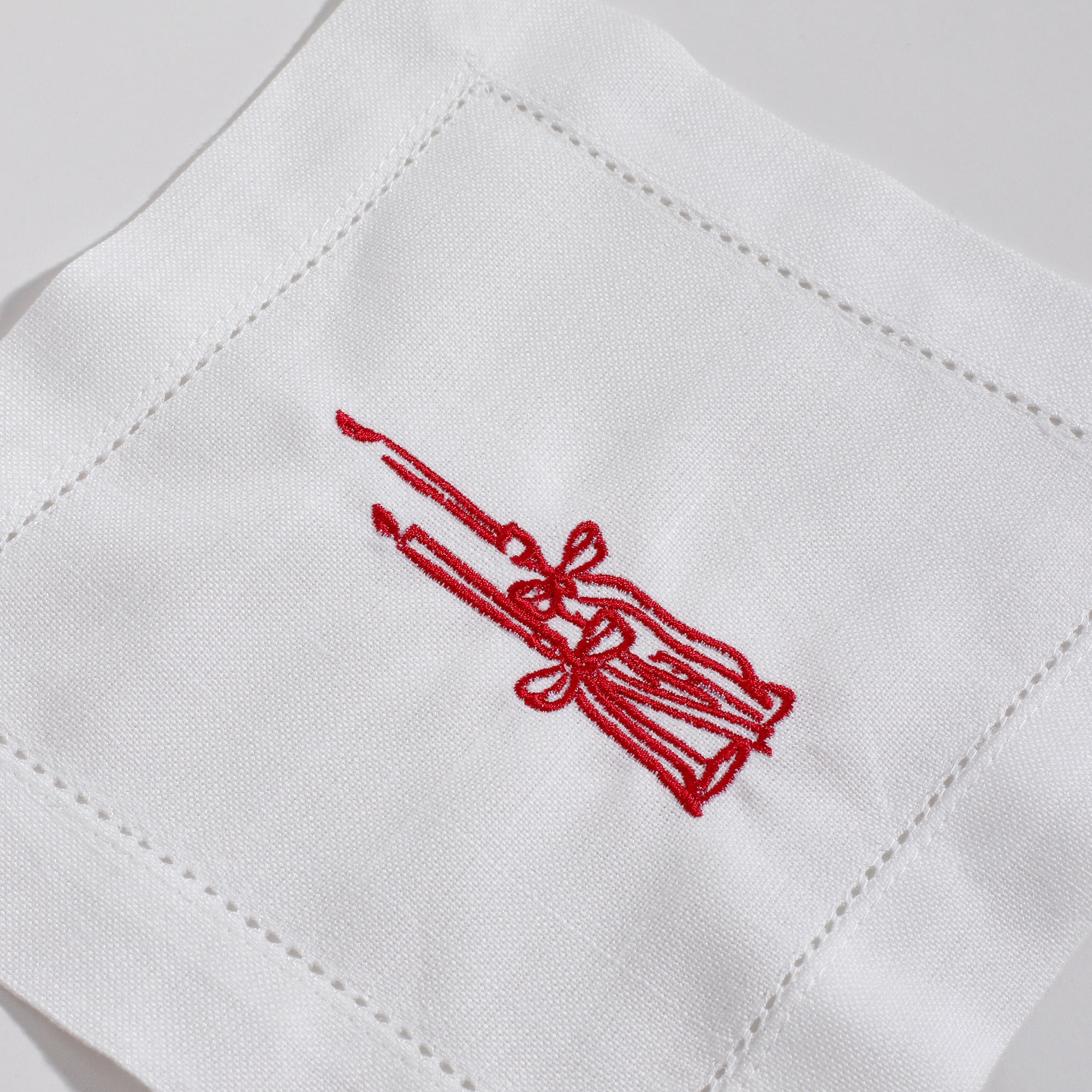 White fabric with red embroidered design of a broom and wreath on a white background