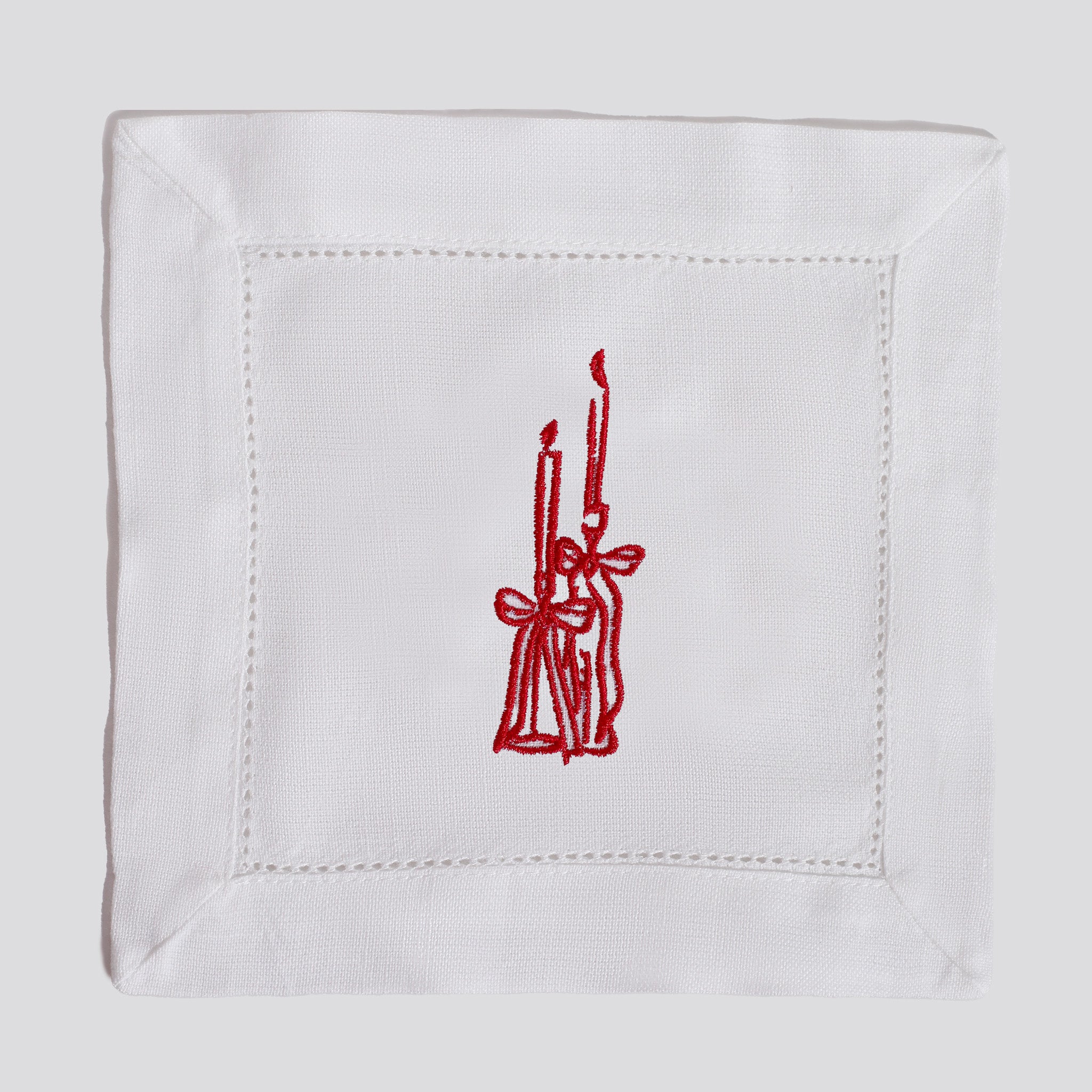 White napkin with red embroidered design of candles and a bow on a white background