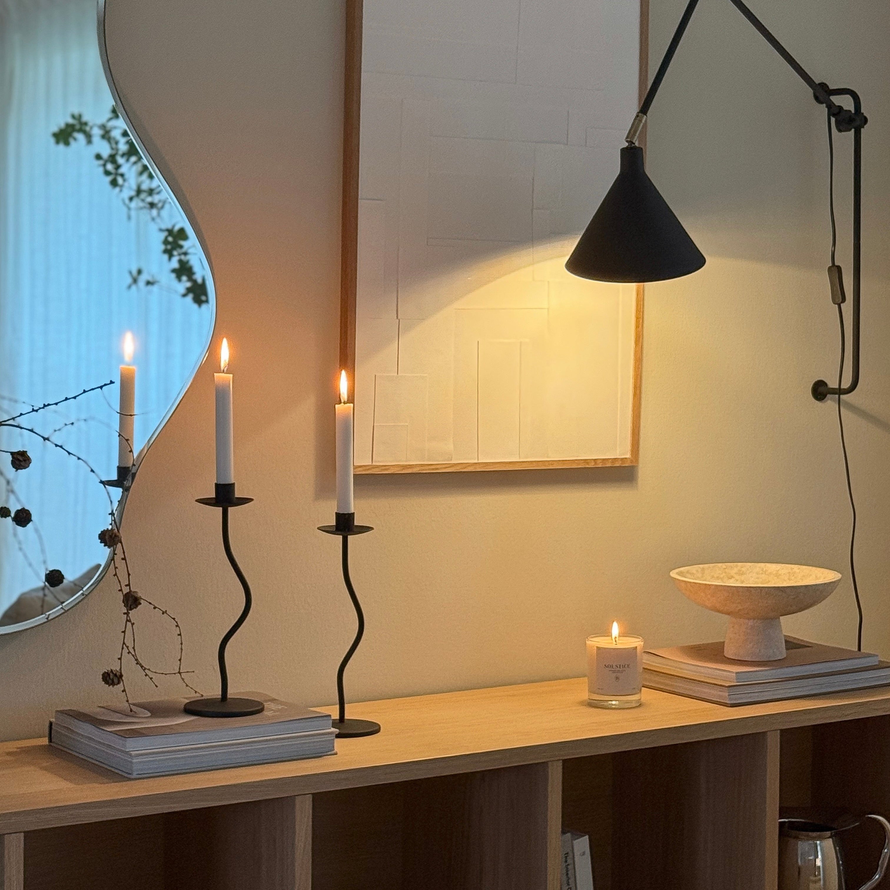 Minimalist home decor with Boujie candle and curved mirror, featuring soft lighting and black candlesticks on wooden console.