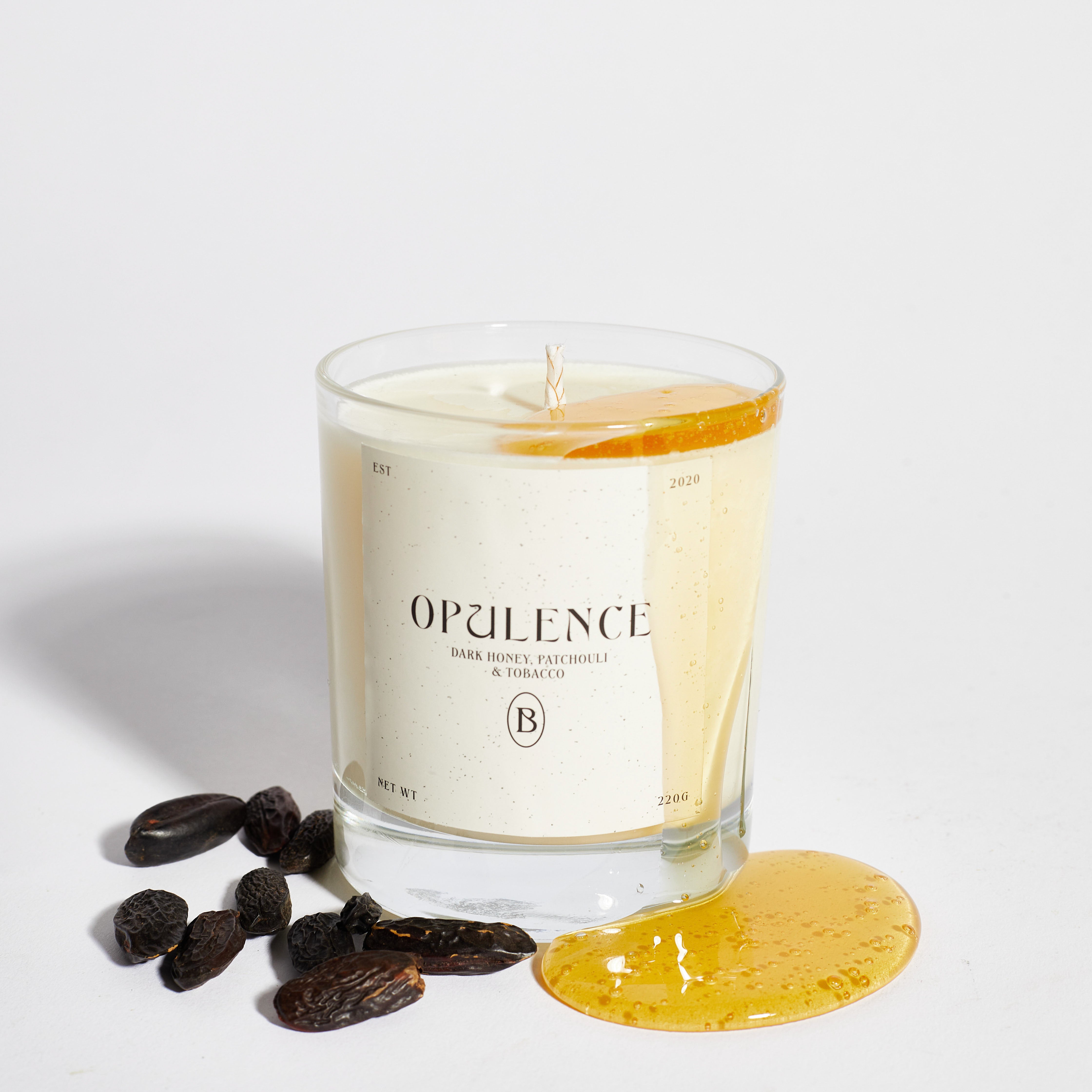 Boujie Opulence luxury soy wax jar candle, front view, handmade with natural soy wax in clear glass jar, scented with dark honey, patchouli, and tobacco, styled with honey drizzle and tonka beans.