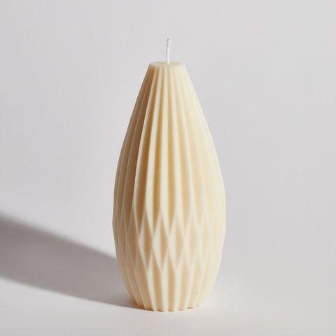 A cream-colored decorative candle with a geometric pattern, designed to resemble a lantern, on a plain background.
